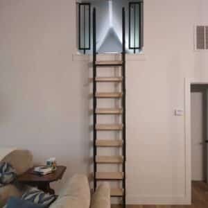 A 10 Foot Loft Ladder with sleek black metal sides leads to an elevated loft opening in a pristine white wall. Below, a beige couch decorated with patterned pillows is next to an item-laden side table. A door and vent on the right add symmetry to the space.
